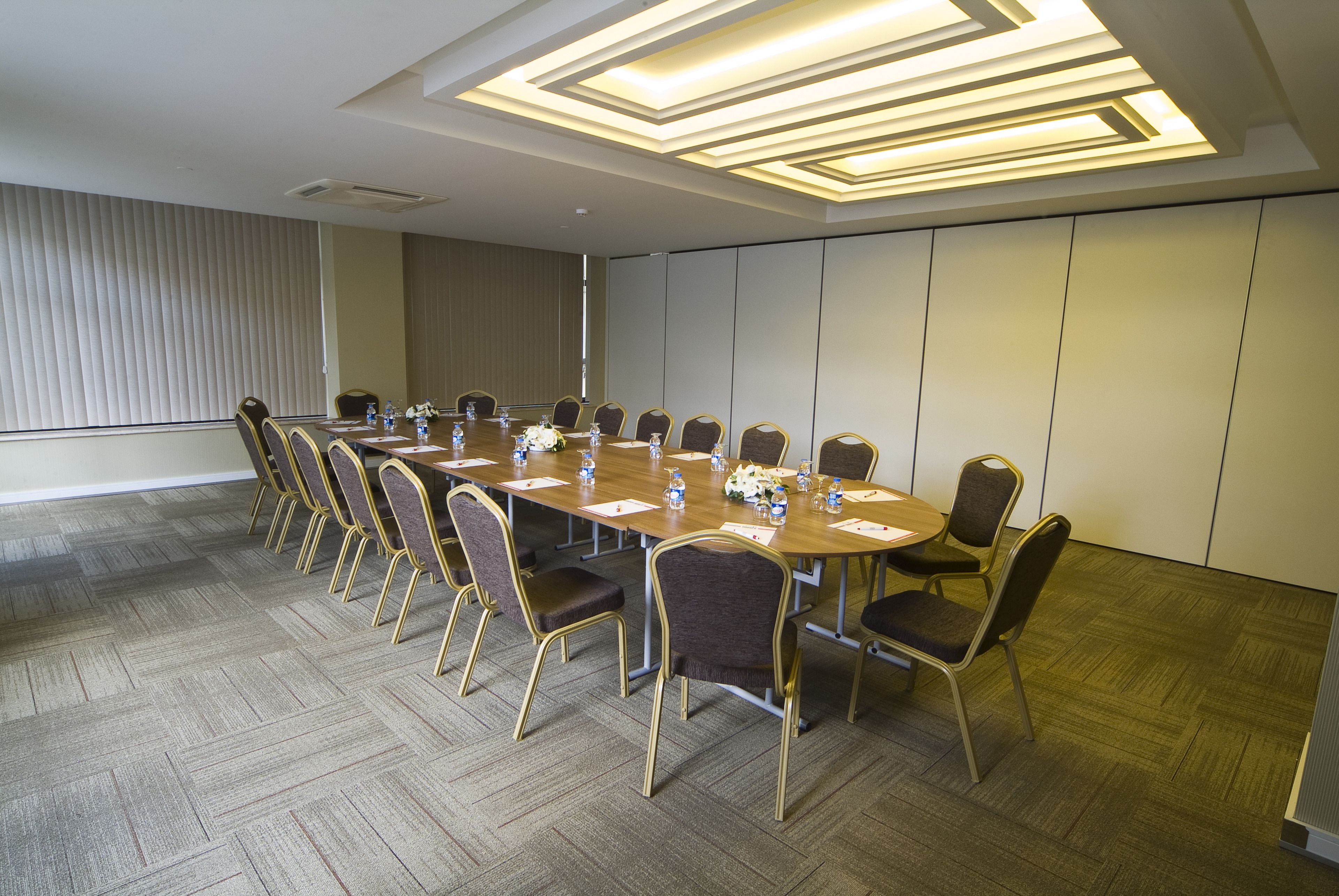 Une salle de conférence avec une longue table, des chaises, des bouteilles d’eau et un arrangement floral au centre.