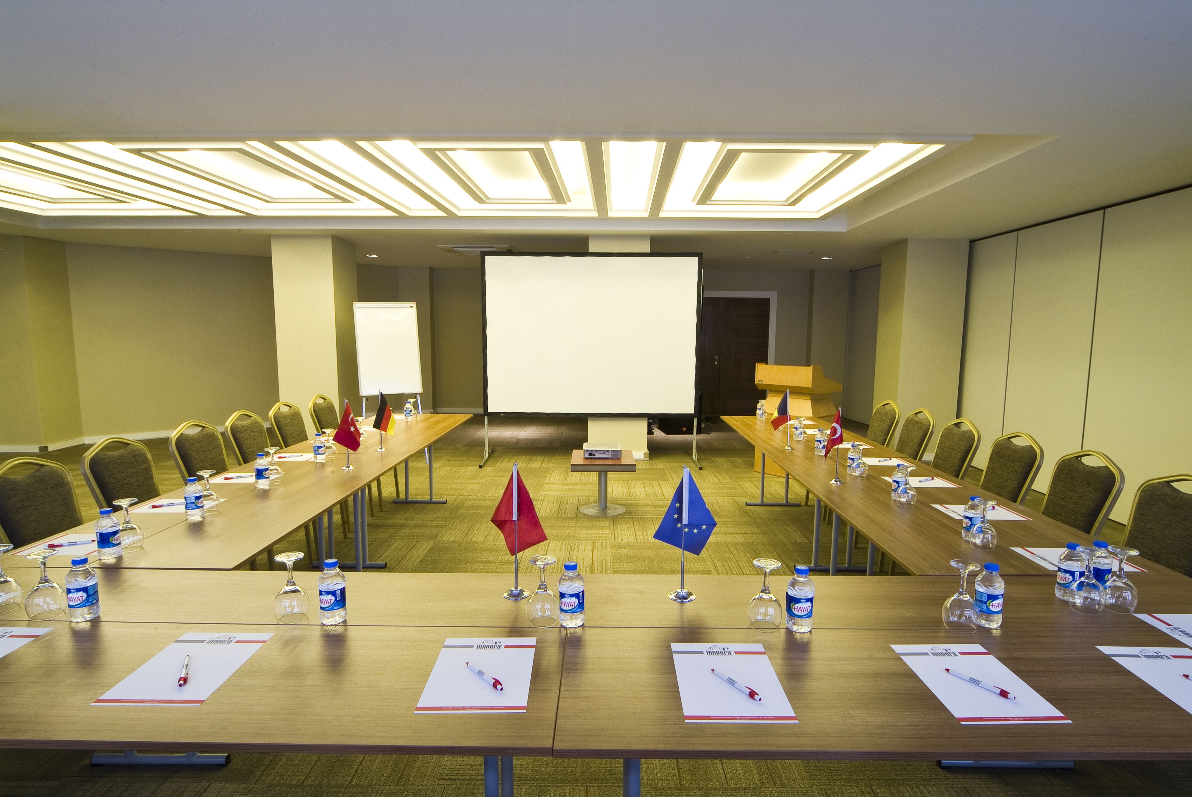 A conference room with a long table, chairs, water bottles, name tags, and flags.