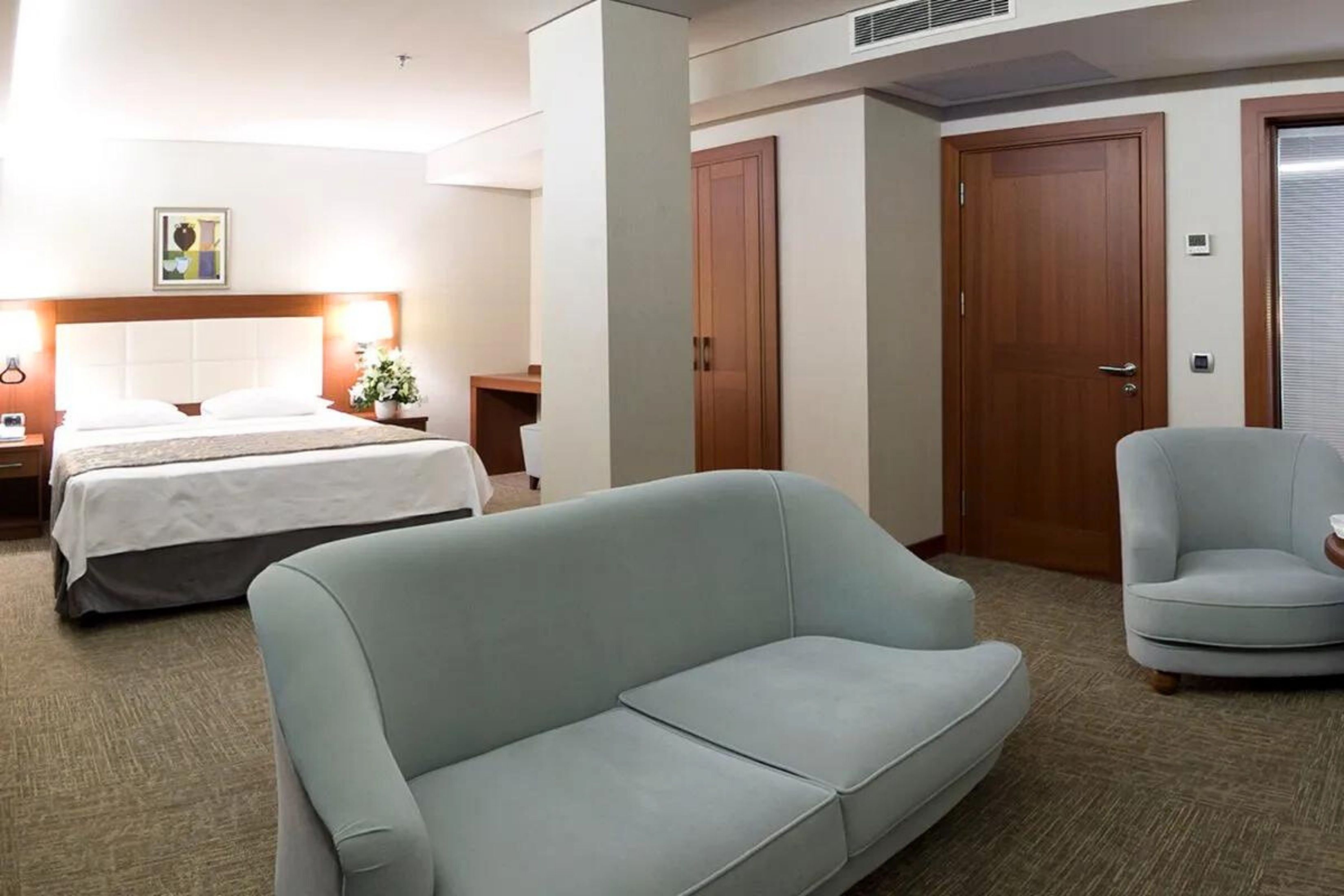 Ein Hotelzimmer mit einem Bett, einem Schlafsofa, einem Sessel, einem Nachttisch und einer Wand-Klimaanlage.