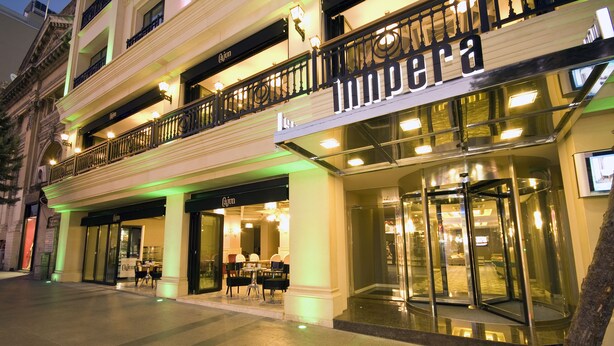 Un hotel con una entrada destacada, puerta de cristal y un balcón con barandillas.