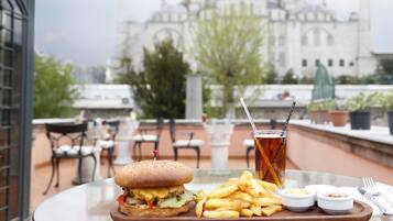 Un plateau repas contenant un hamburger, des frites et des accompagnements, posé sur une table avec, en arrière-plan, la vue d’un immeuble.
