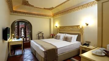 Une chambre d’hôtel avec un grand lit, un bureau avec une lampe, une chaise et une petite table avec une tasse et une soucoupe.
