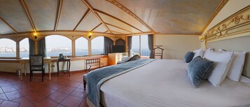 Habitación de hotel con una cama grande, un escritorio con una silla, un televisor y vistas a la ciudad a través de amplias ventanas.