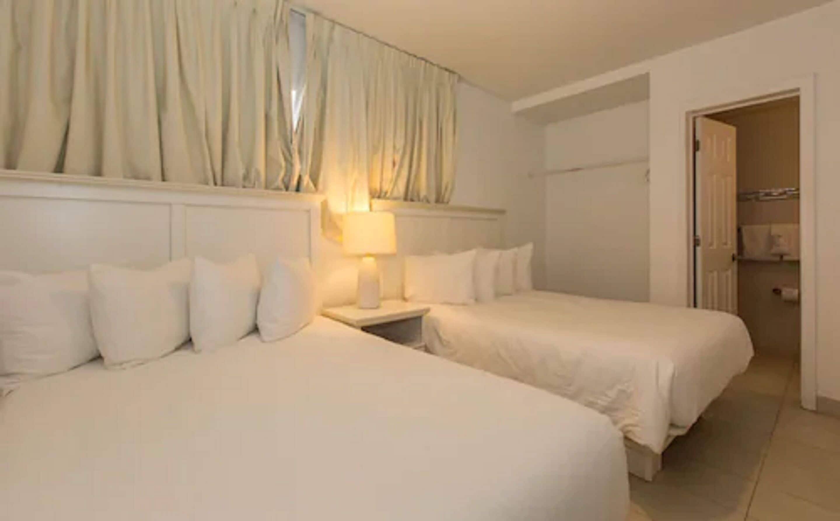 Een hotelkamer met twee bedden, een nachtkastje met een lamp, en uitzicht op een badkamer met douche en toilet.