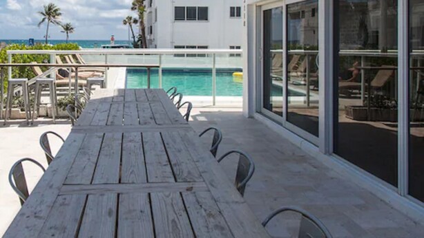 A wooden deck with a pool table and chairs, overlooking a pool and a building with large windows. - Premiere Hotel (Fort Lauderdale)