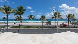 A beachside view with palm trees, a road, and a beach with people and cars. - Premiere Hotel (Fort Lauderdale)