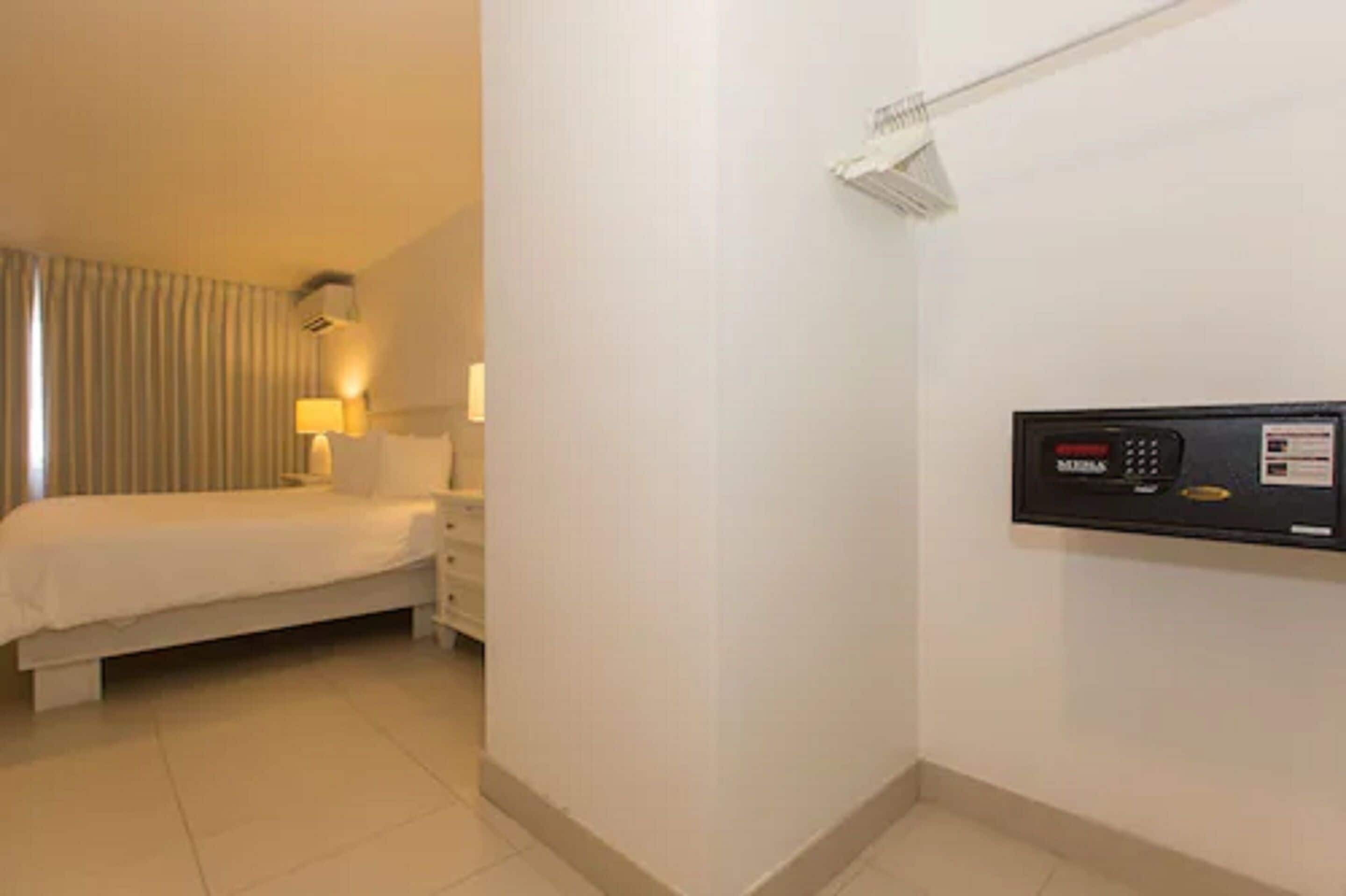 Een hotelkamer met een bed, nachtkastje, lamp en een bedieningspaneel aan de muur.