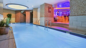Ein Hallenbad mit klarem Wasser, gefliesten Wänden und einem Empfangsbereich mit Theke und Sitzgelegenheiten.