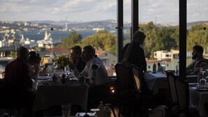 Ein Restaurant mit gedeckten Tischen, Blick auf eine Brücke und die Skyline, und ein Kellner, der sich um die Gäste kümmert.
