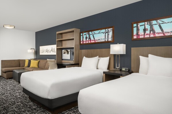A hotel room with two beds, a sofa, a TV, a desk, and artwork on the walls.
