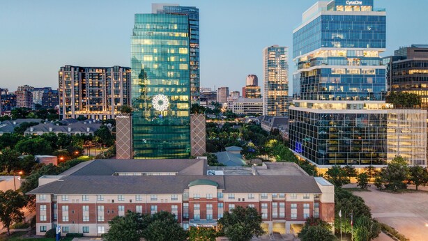 A modern hotel with a glass facade, a central clock tower, and a parking lot.