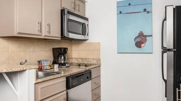 A kitchen with a microwave, coffee maker, dishwasher, and a painting on the wall.