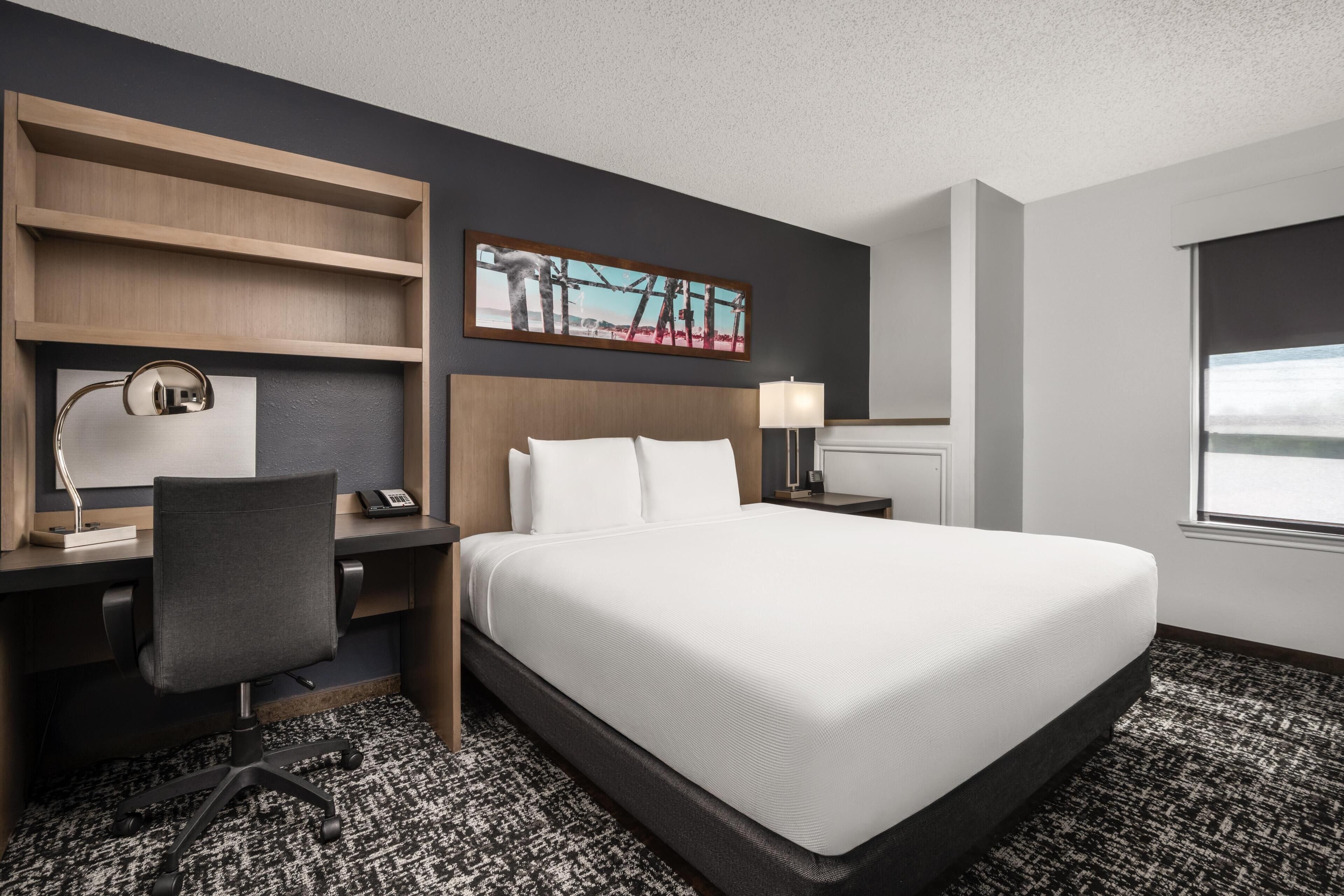 Une chambre d’hôtel avec un lit, un bureau, une chaise et un tableau au mur.