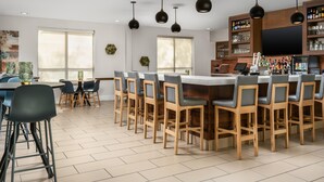 A modern bar area with a long counter, multiple bar stools, and pendant lighting.