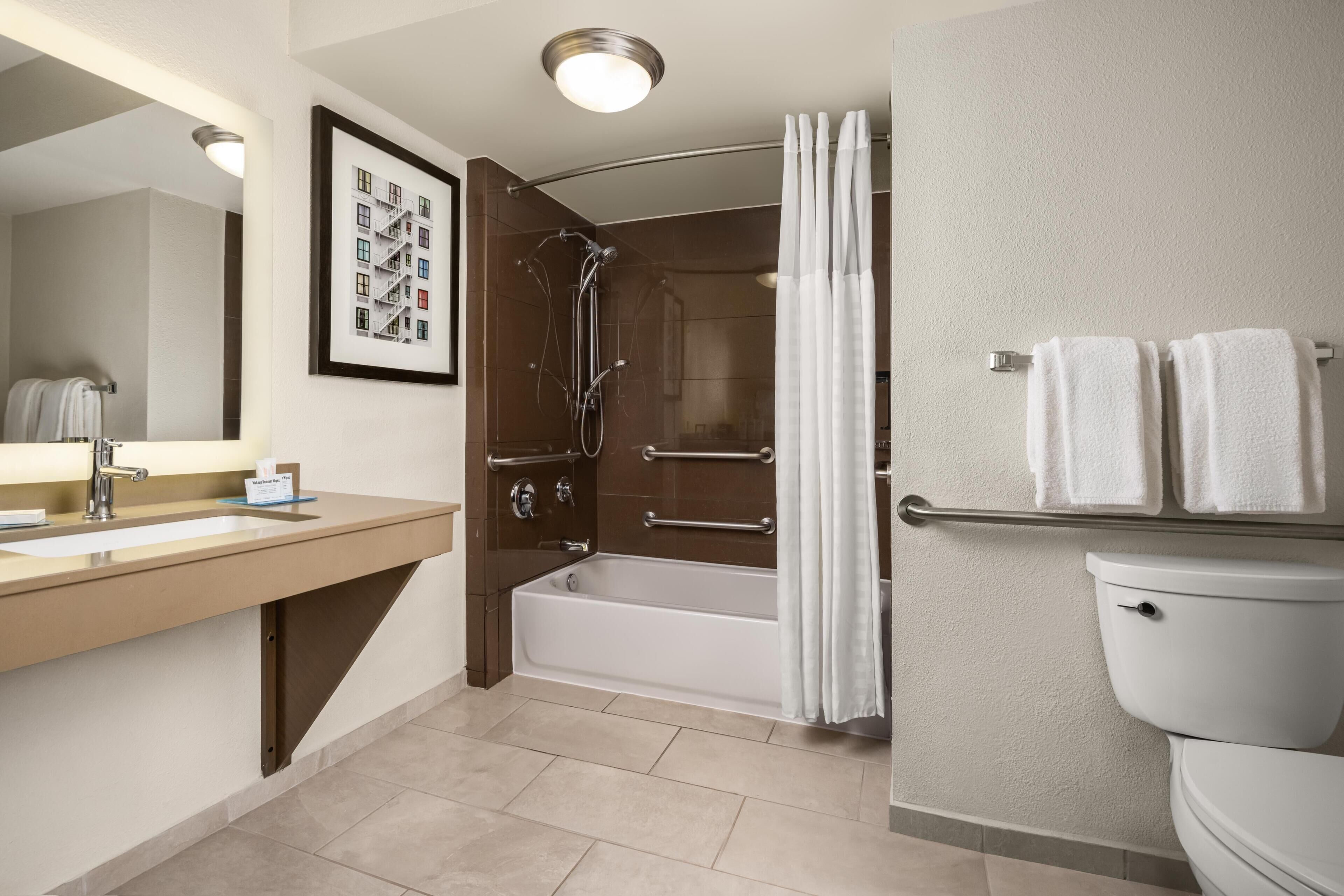 A modern bathroom with a sink, mirror, bathtub, shower, and toilet.