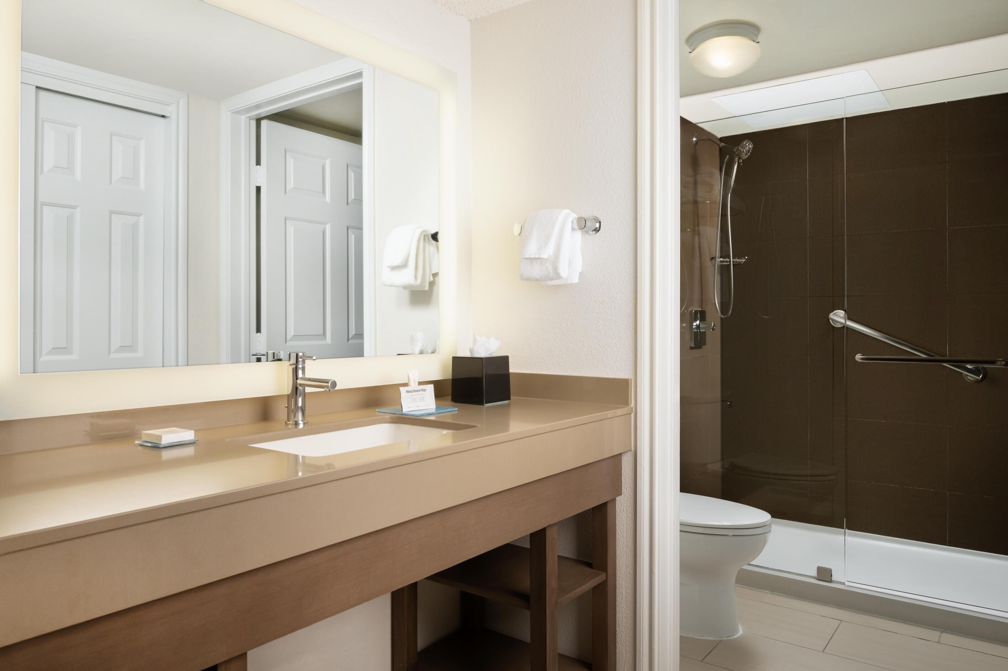 A bathroom with a sink, mirror, towel rack, and a shower area.