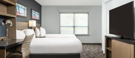 Habitación de hotel con cama, escritorio, silla, televisor y una obra de arte en la pared.