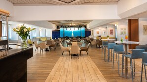 Un vaste espace dédié à la salle à manger, avec de nombreuses tables et chaises, une scène centrale dotée d’un décor bleu et un plafond en bois.
