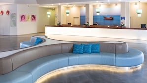 Un hall d’hôtel moderne avec un espace salon aux lignes courbes, un comptoir d’accueil et un grand miroir qui reflète l’intérieur.