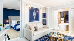 Une chambre d’hôtel moderne avec un lit, un canapé, une table basse en verre et une grande fenêtre.