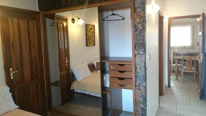 Quarto com cama, guarda-roupa de madeira e uma pequena escrivaninha com gavetas.