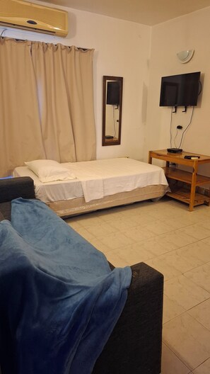 A hotel room with a bed, a TV, a wooden side table, and a mirror. - Apar-T-Hotel Porta Westfalica (Asunción)