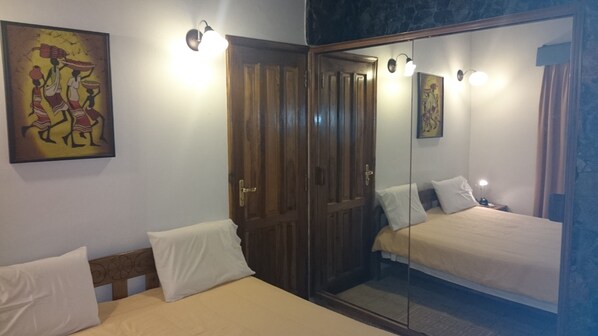 A room with two beds, a wardrobe, and a mirror.