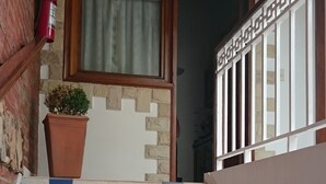 Uma escadaria com azulejos alternados em bege e azul, um vaso de planta, um extintor de incêndio e uma porta de madeira com um vitral acima.