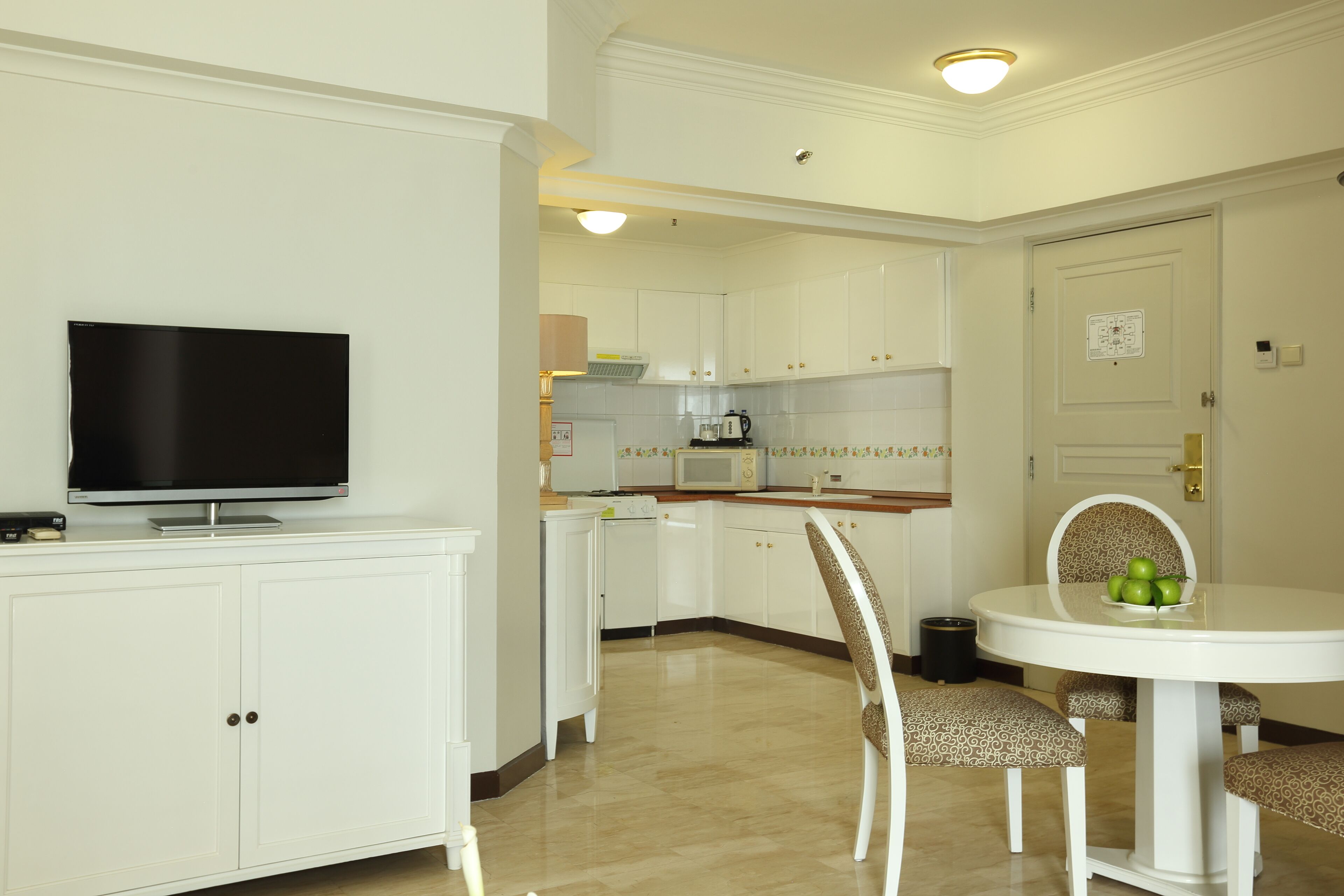 A modern kitchen with white cabinets, a flat-screen TV, a microwave, and a dining area with a table and chairs.