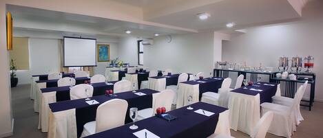 A conference room with multiple tables, white chairs, and a projector screen.