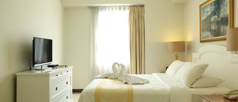 A hotel room with a bed, a TV on a dresser, a painting on the wall, and a window with curtains.