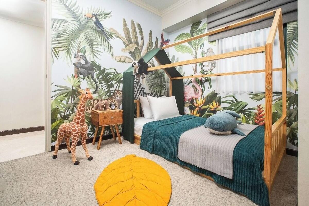 A child's bedroom with a bed, a wooden play structure, and a mural of jungle animals.