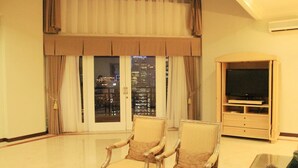 A spacious living room with two armchairs, a flat-screen TV on a wooden stand, and a large window with curtains. - Aryaduta Suites Semanggi (Jakarta)
