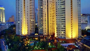 A high-rise building complex with multiple floors, surrounded by greenery and a tennis court. - Aryaduta Suites Semanggi (Jakarta)