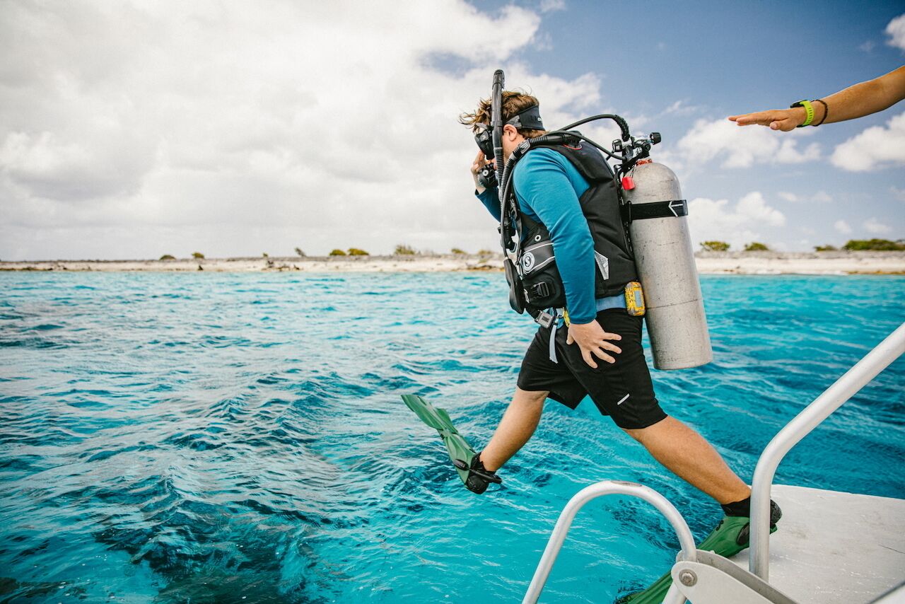 A person in scuba gear stepping off a boat onto a clear blue sea.