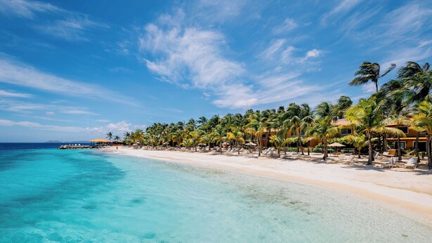 Um resort à beira-mar com águas turquesa cristalinas, palmeiras e guarda-sóis.