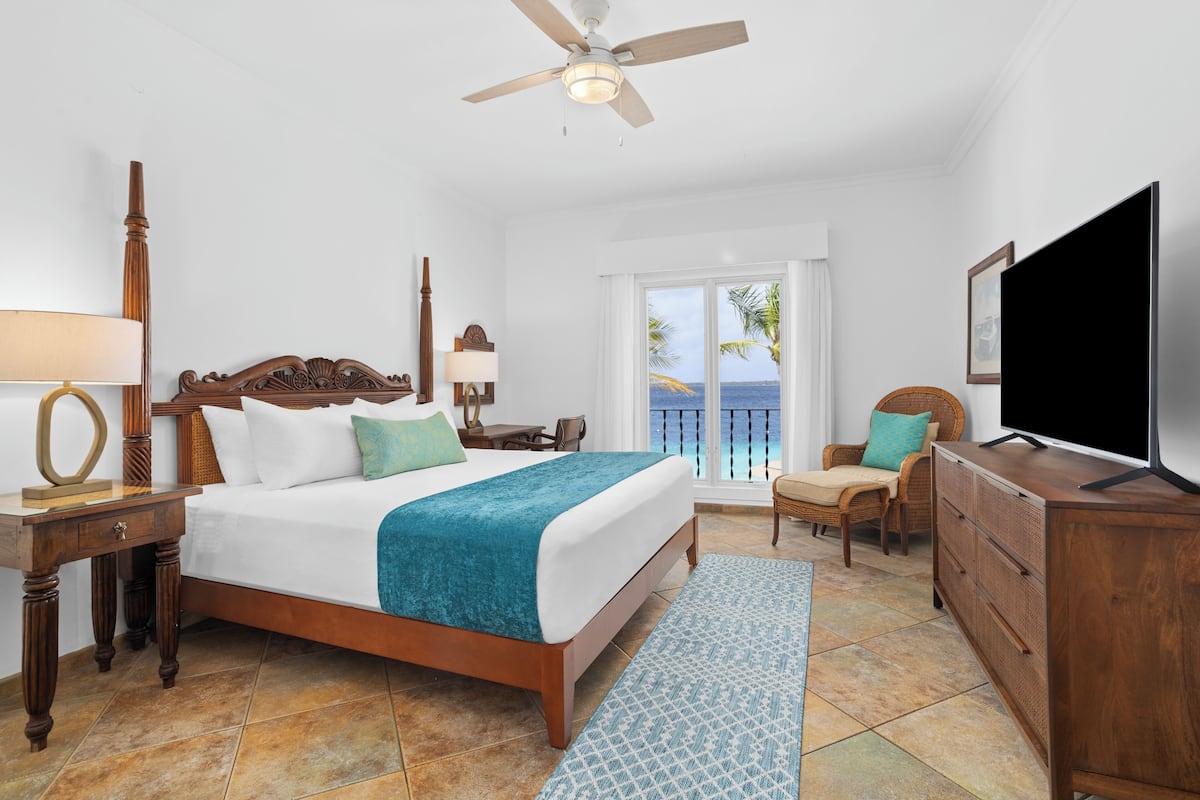 A hotel room with a bed, a television, a desk, a chair, a dresser, and a balcony with a view.