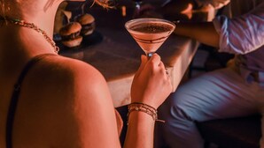 Uma pessoa segurando um drink em um bar com vista para o oceano.