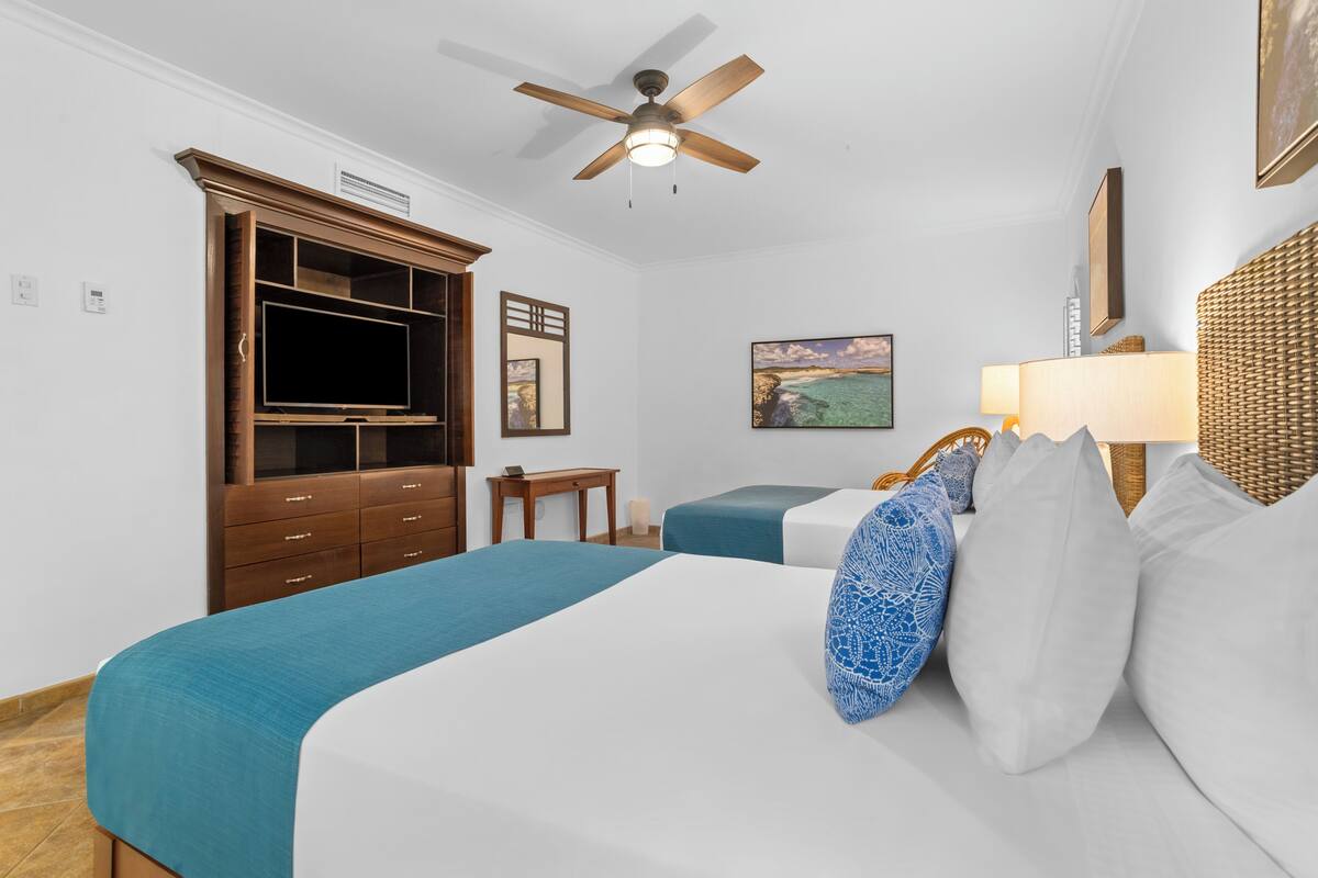 A hotel room with a bed, a desk, a television, a wardrobe, and a ceiling fan.