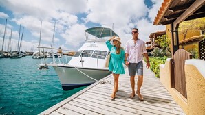 Um casal caminhando em um píer de madeira com um barco chamado 'Great Adventures' atracado perto.