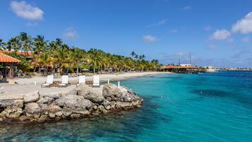A beachfront resort with a stone pier, lounge chairs, and palm trees.