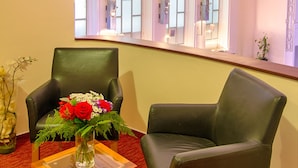 Ett rum med två läderfåtöljer, ett glasbord med en vas med blommor och utsikt över välvda fönster med kristallkronor.