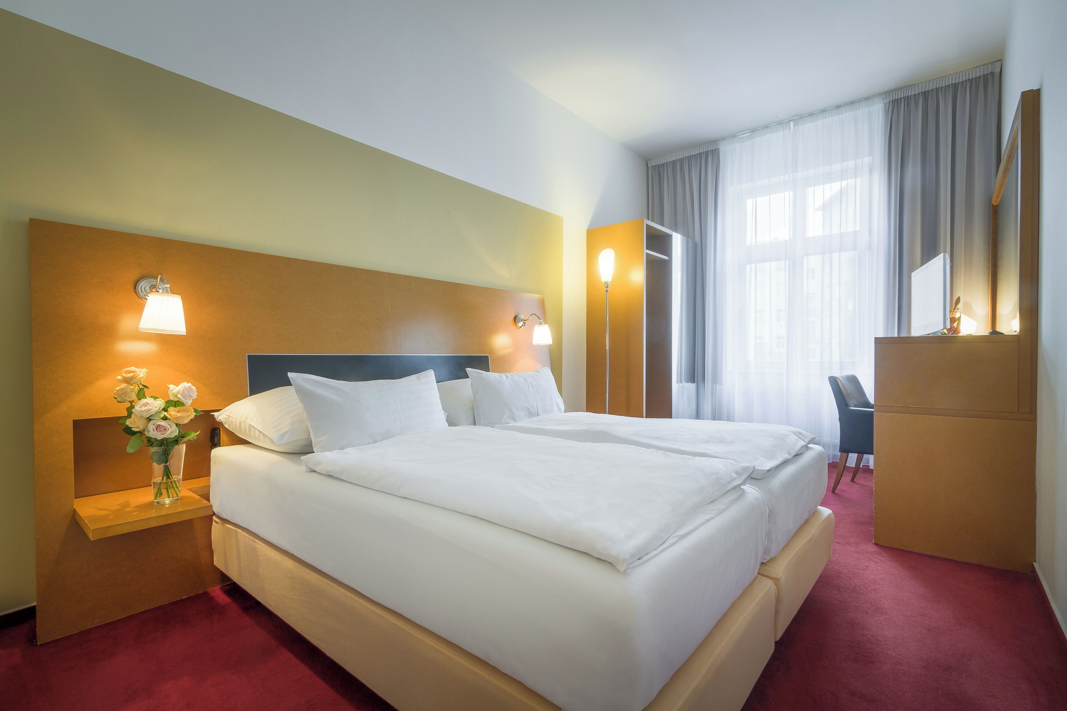 Een hotelkamer met een groot bed, nachtlampen, een bureau en een spiegel.