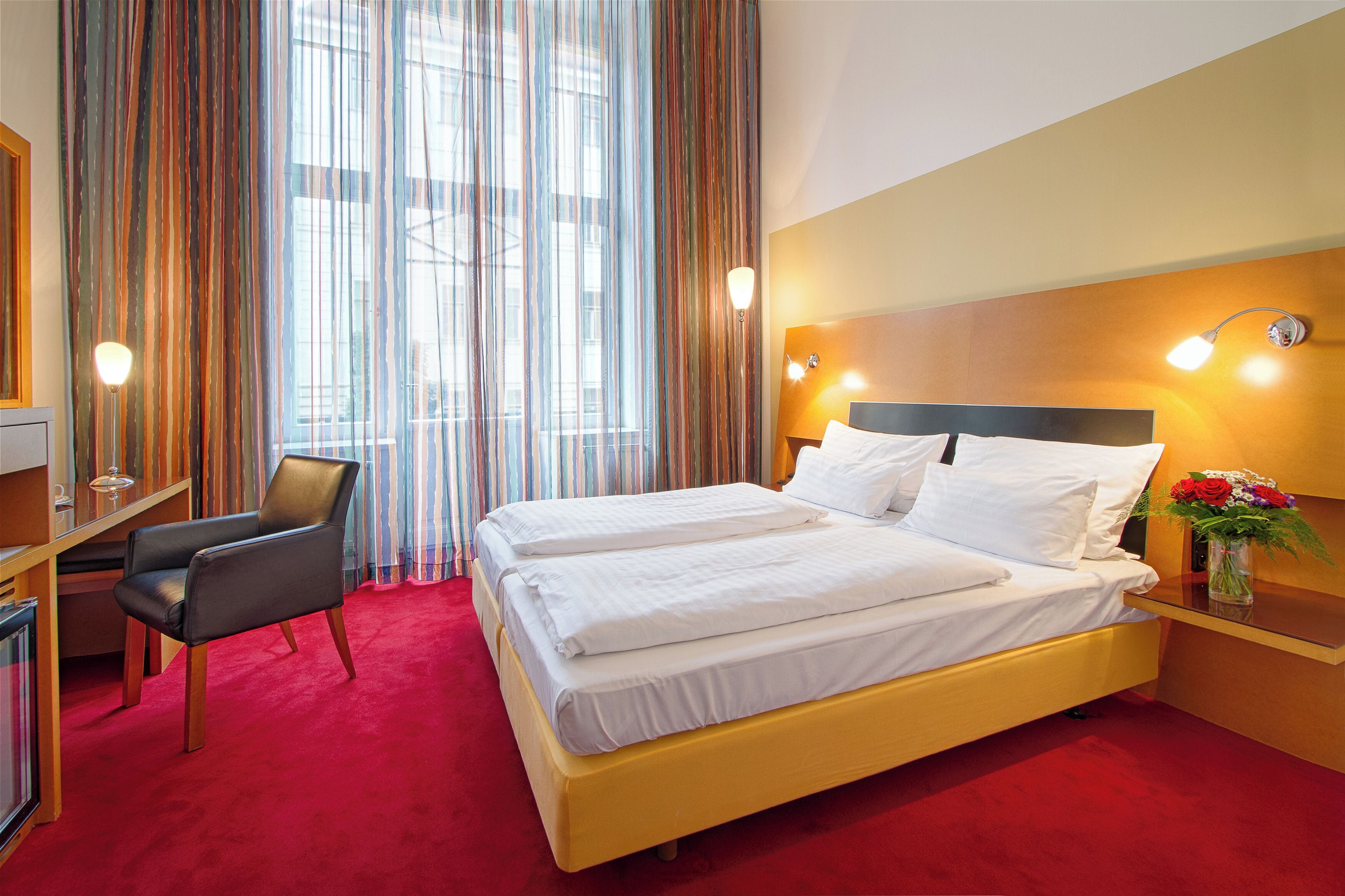 Een hotelkamer met een tweepersoonsbed, een bureau met stoel, een boekenkast en een raam met gordijnen.