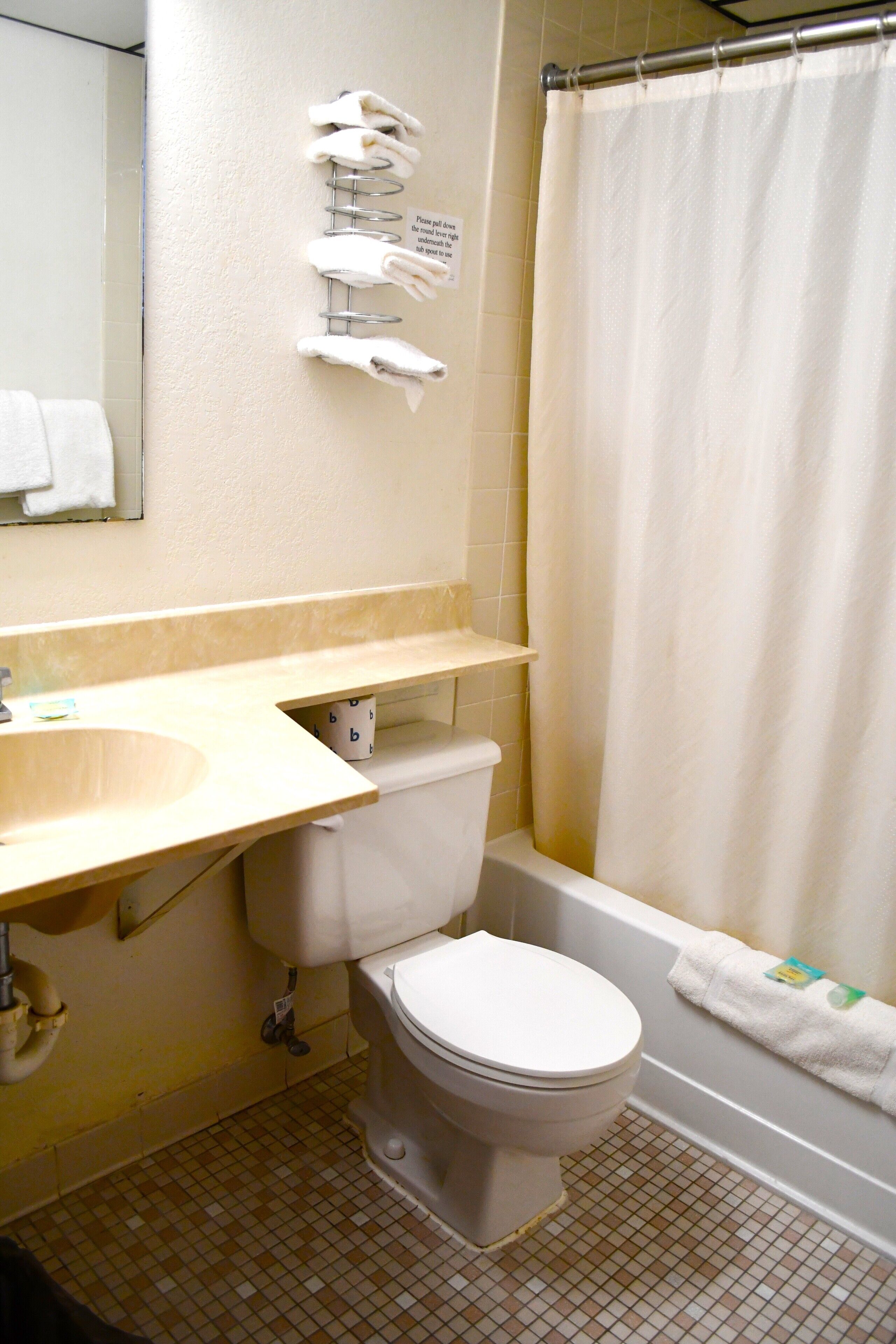 A bathroom with a toilet, sink, and bathtub. There is a towel rack with towels and a sign above it.