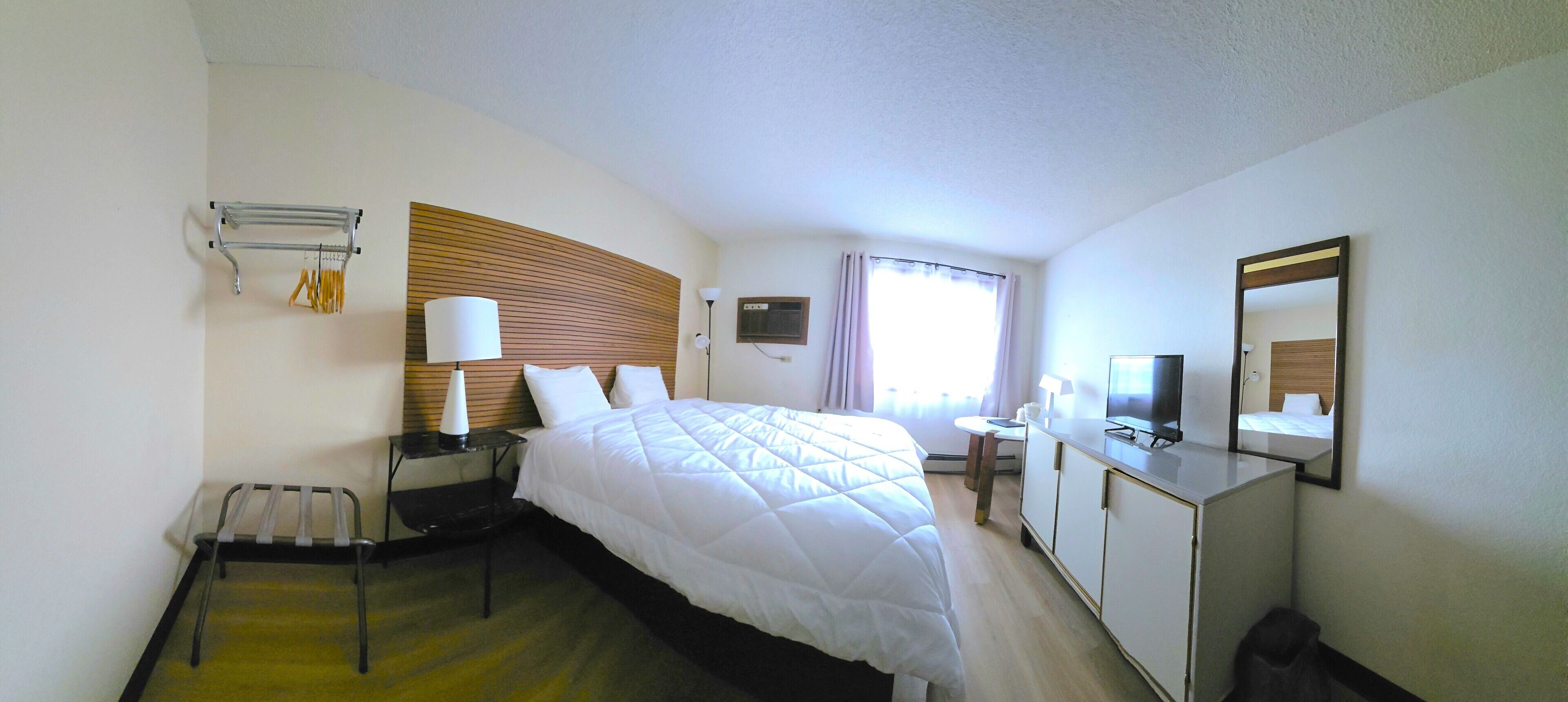 Una habitación de hotel con cama, mesita de noche, lámpara, armario y espejo.