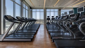 Un gimnasio con cintas de correr alineadas a lo largo de las paredes, ventanas amplias y suelo de madera.