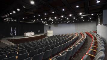 Een auditorium met rijen stoelen, een podium en een speakersysteem.