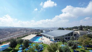 Un hotel moderno con una amplia piscina, un espacio exterior cubierto y vistas a la ciudad al fondo.