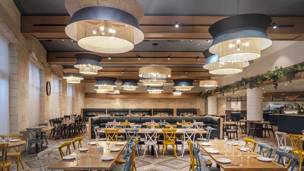 Un restaurante espacioso con varias zonas de comedor, incluyendo una mesa común grande y varias mesas más pequeñas.